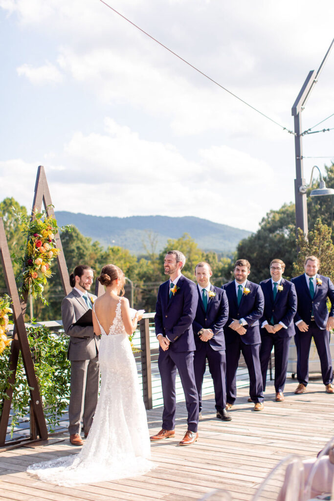 A wedding couple exchanging vows with their wedding parties behind them 