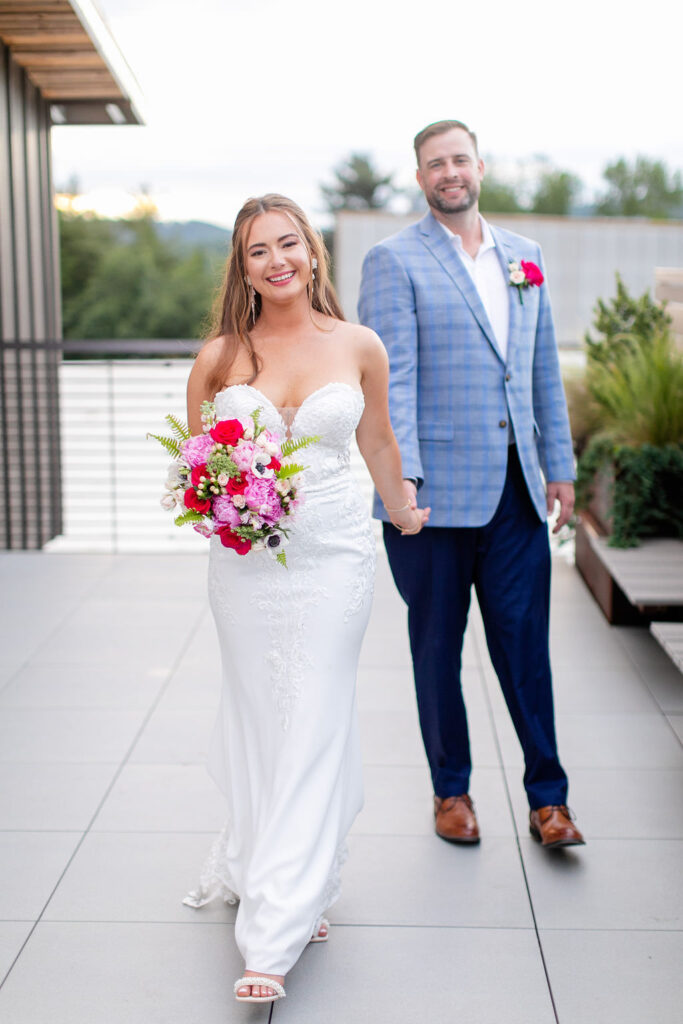 A wedding couple holding hands and walking along a rooftop 