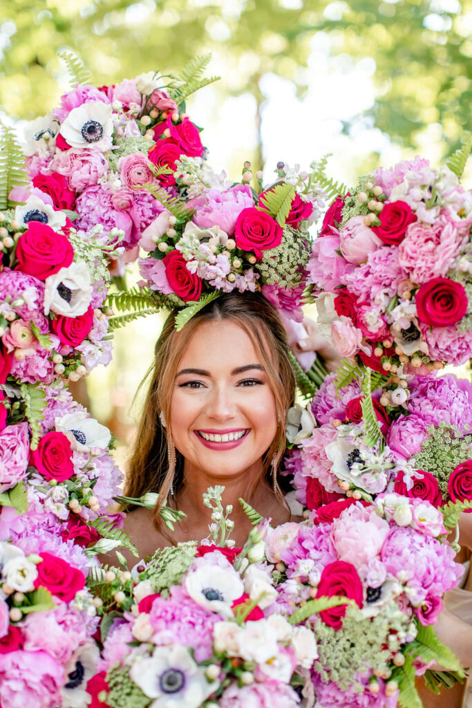 A person smiling with a heart shaped flower arrangement in front of their face 