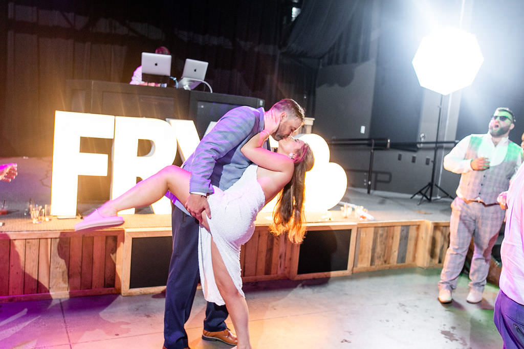 A groom dipping a bride at their wedding reception as they kiss 