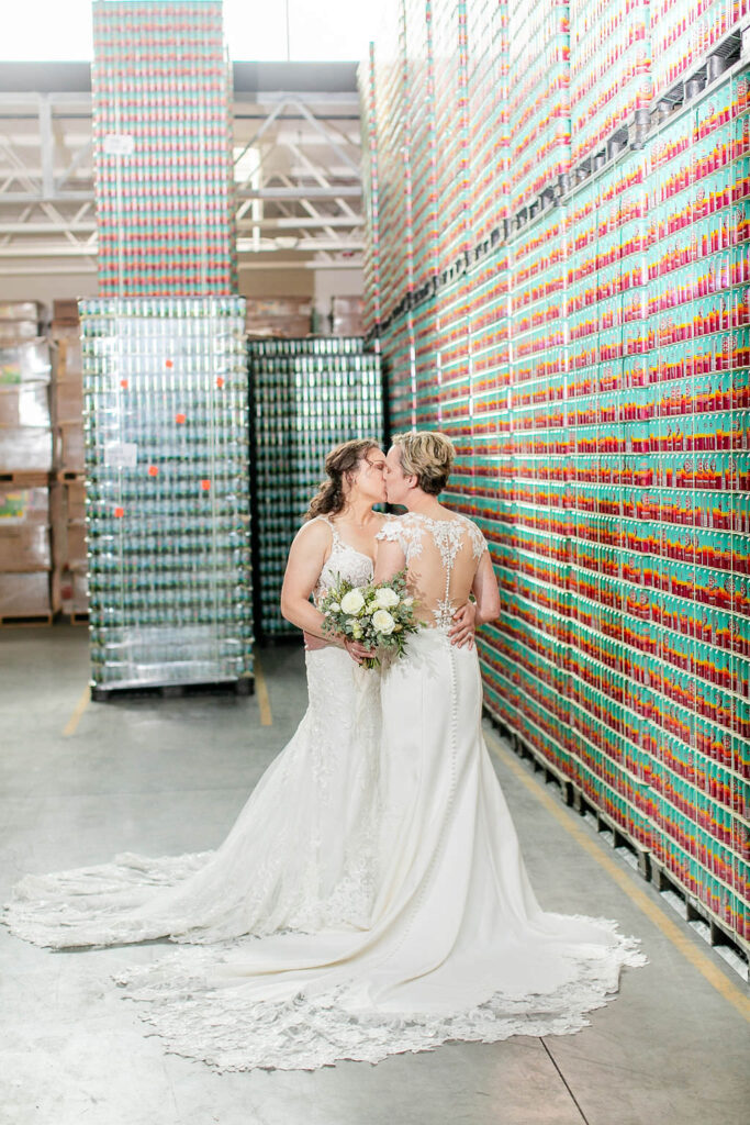 Two brides kissing in front of a colorful beer wall. 