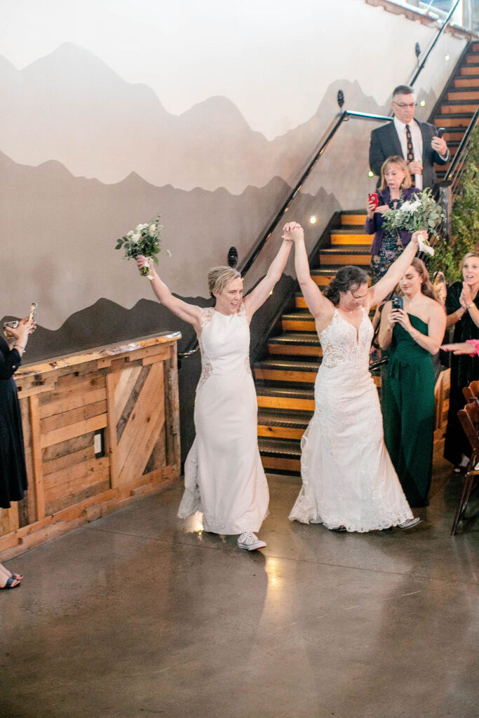 A newlywed couple holding hands and holding them up as they walk into their reception 