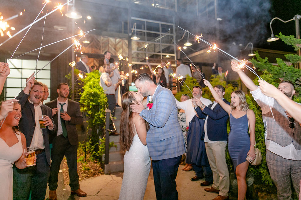 A couple kissing with their guests holding sparklers around them at the end of their Highlands Brewing Company wedding.