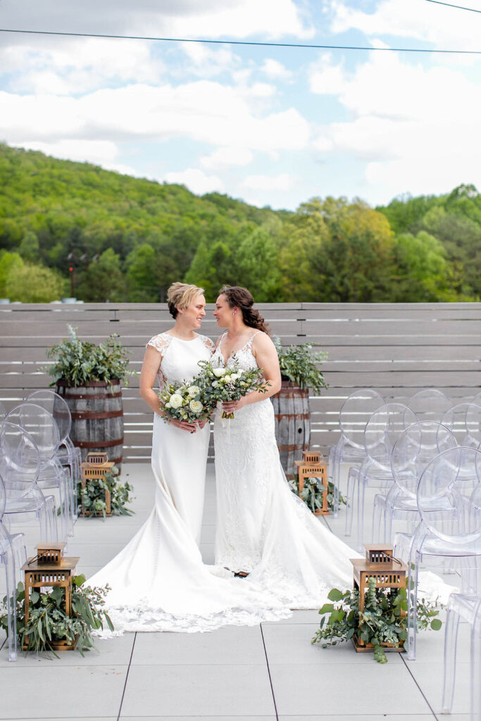 Two brides standing side by side smiling at each other 