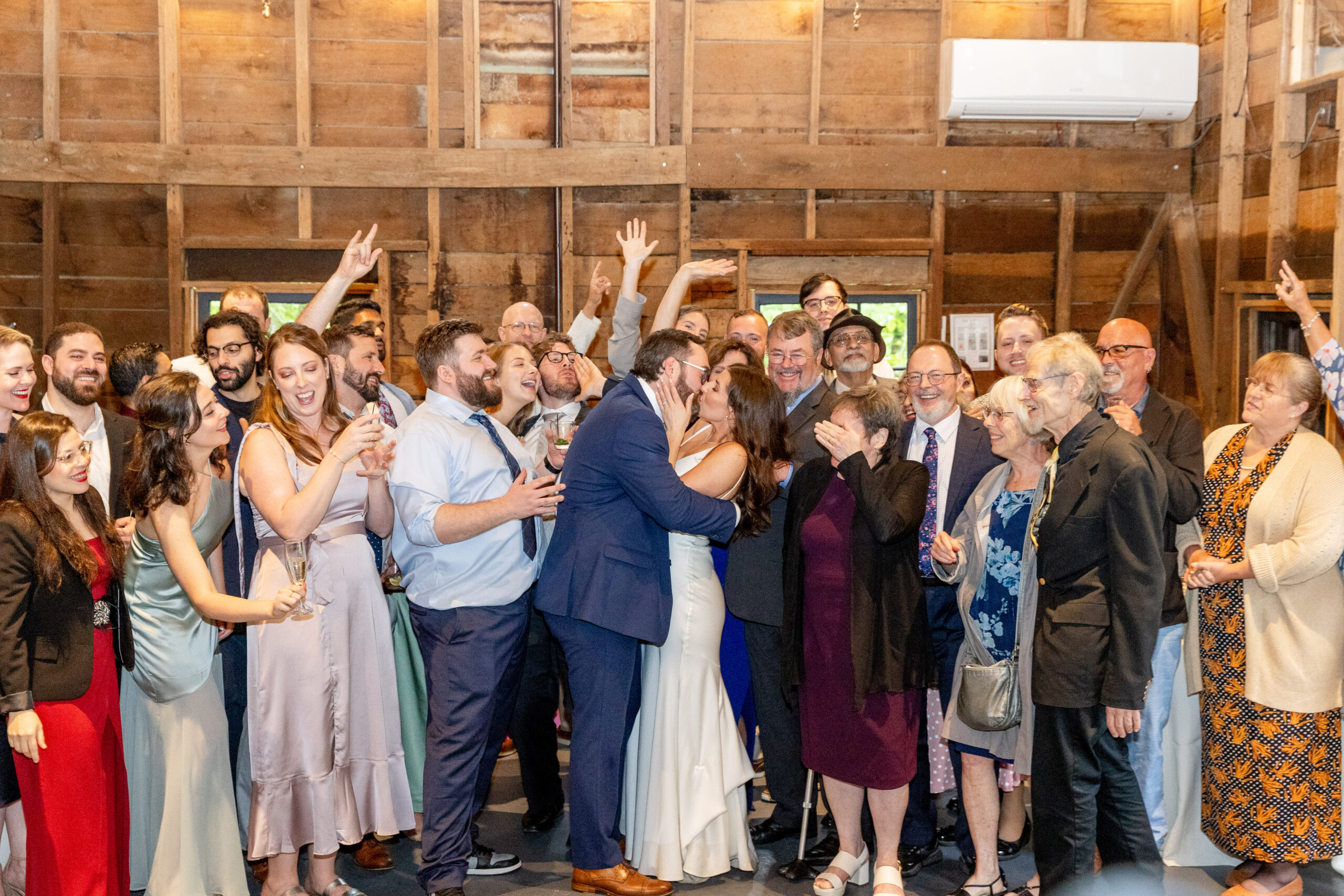 bride and groom kissing at reception with crowd cheering behind them