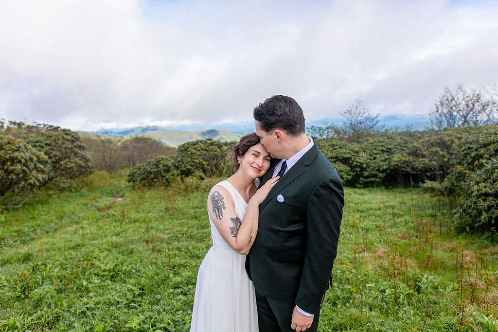 The bride resting her head on the groom’s shoulder, both smiling in a lush outdoor setting.
