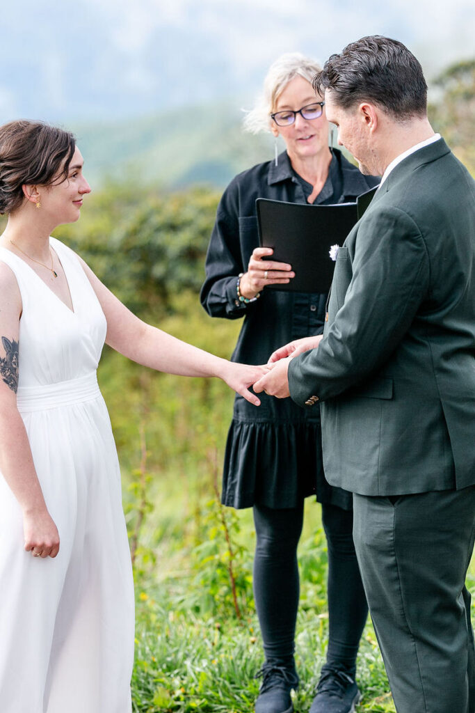 The bride and groom exchanging vows, with the officiant reading from a book in an outdoor setting.
