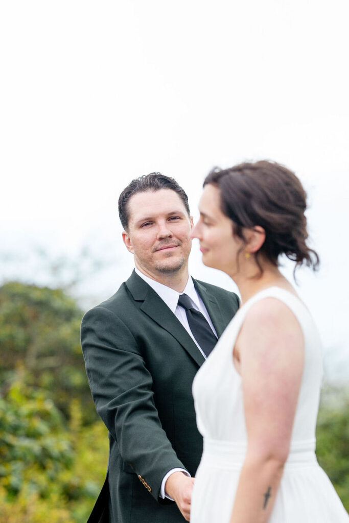 The groom holding the bride’s hand while looking at her 