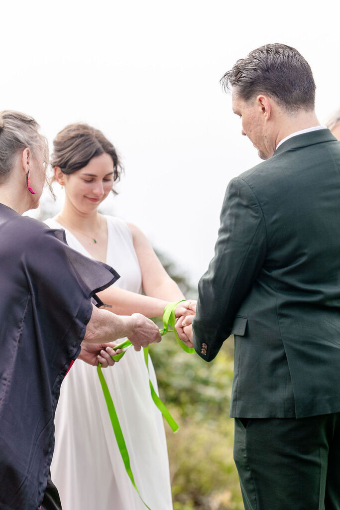 A wedding couple during a handfasting ceremony with one of their guests 