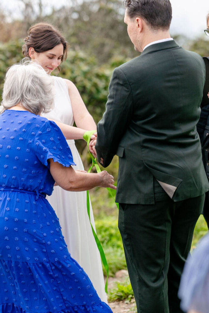 A wedding guests helping a wedding couple during a handfasting ceremony 