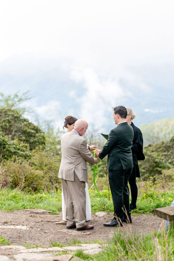 A man tying a ribbon around a wedding couple's hands during their ceremony 