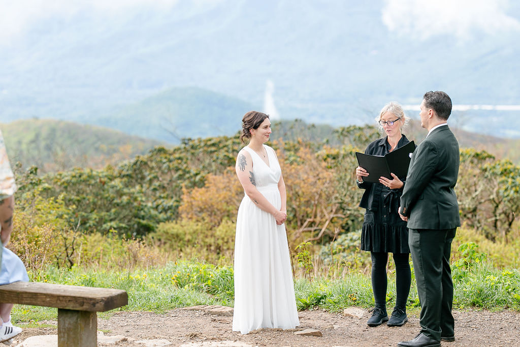 The bride and groom standing with the officiant during their outdoor wedding ceremony with mountains in the background.
