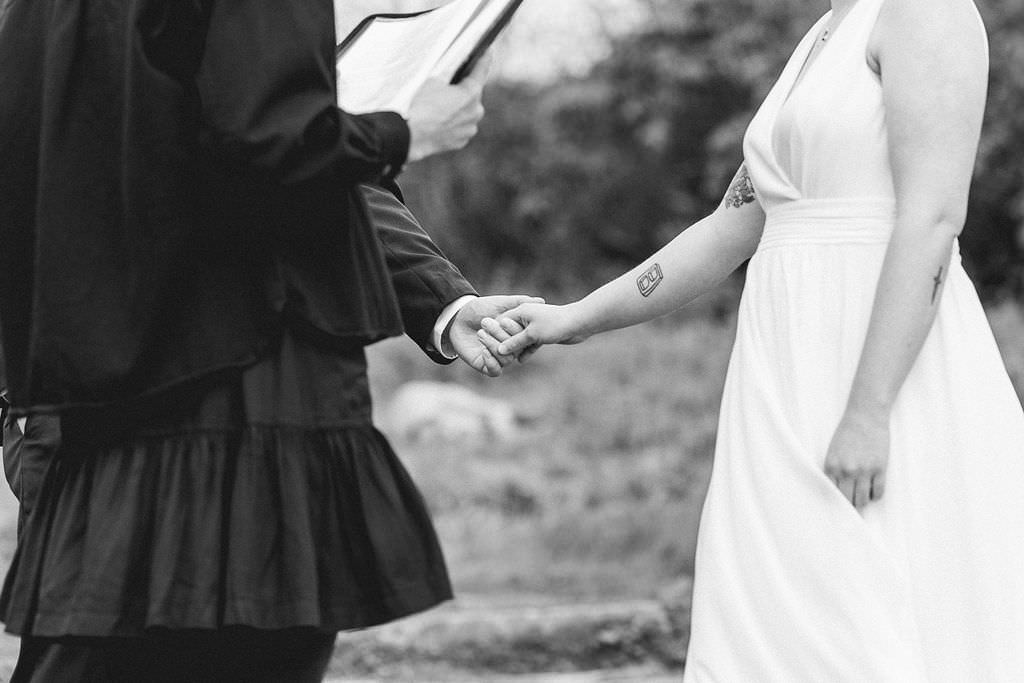 A close-up black-and-white photo of a couple holding hands during their wedding ceremony.
