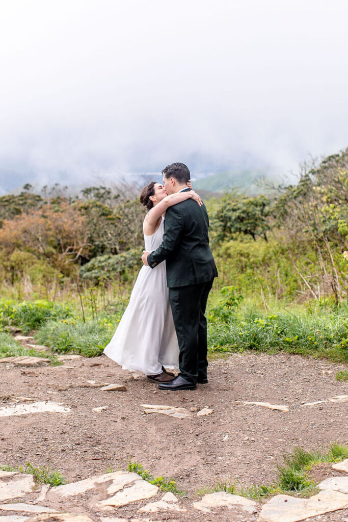 The bride and groom sharing a kiss in a picturesque outdoor setting with a misty mountain view behind them