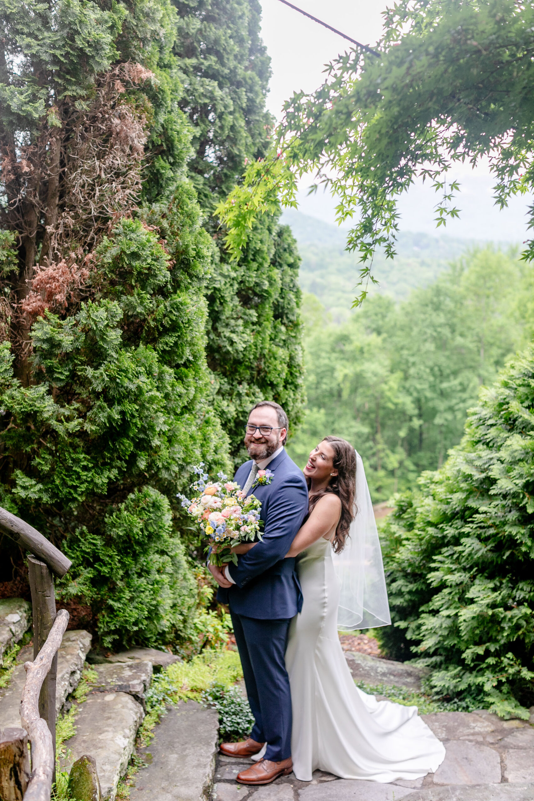 Happy couple bride and groom standing in front of stairs standing in on lush green trees 