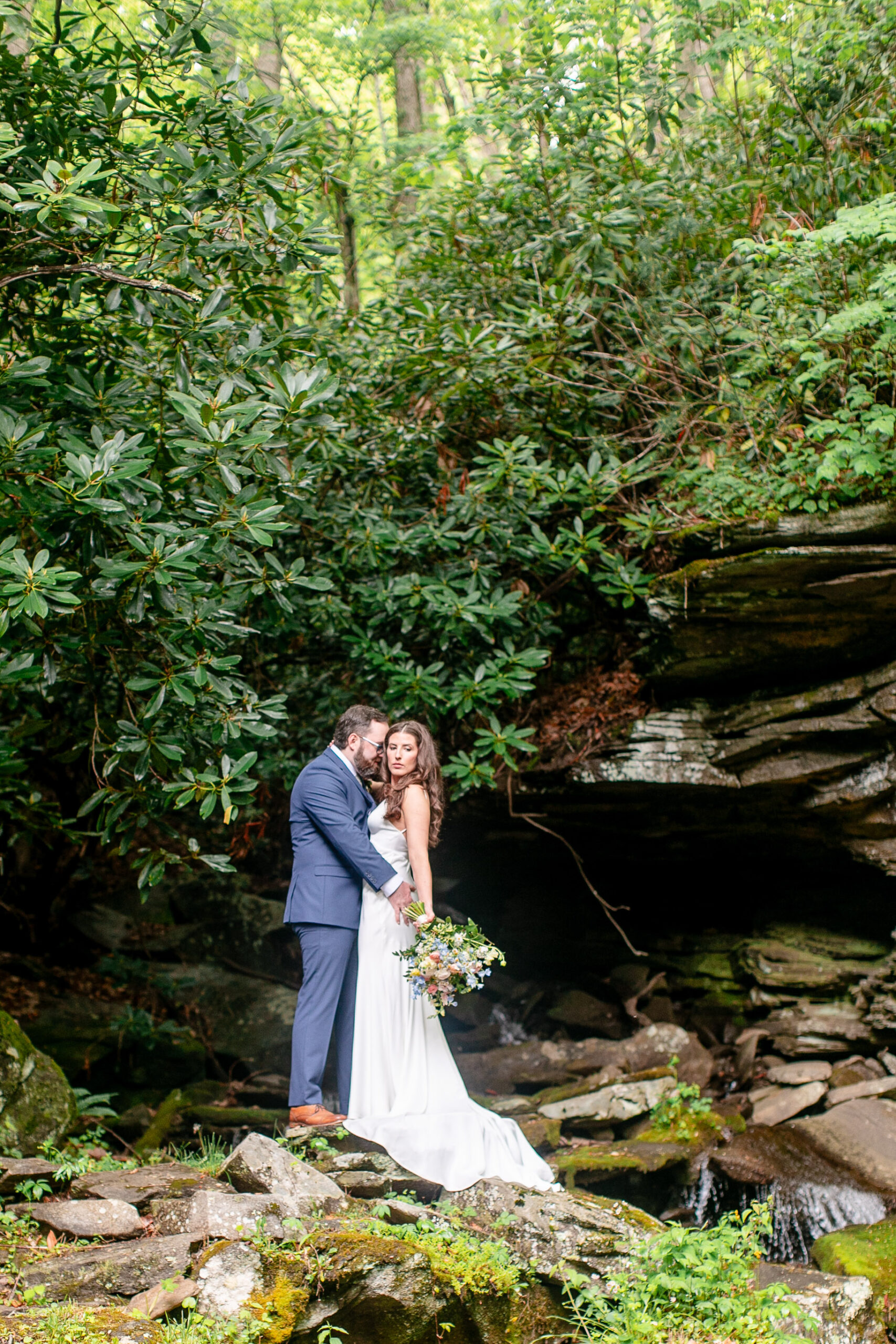 bride and groom standing next to waterfall in laurel falls wedding venue