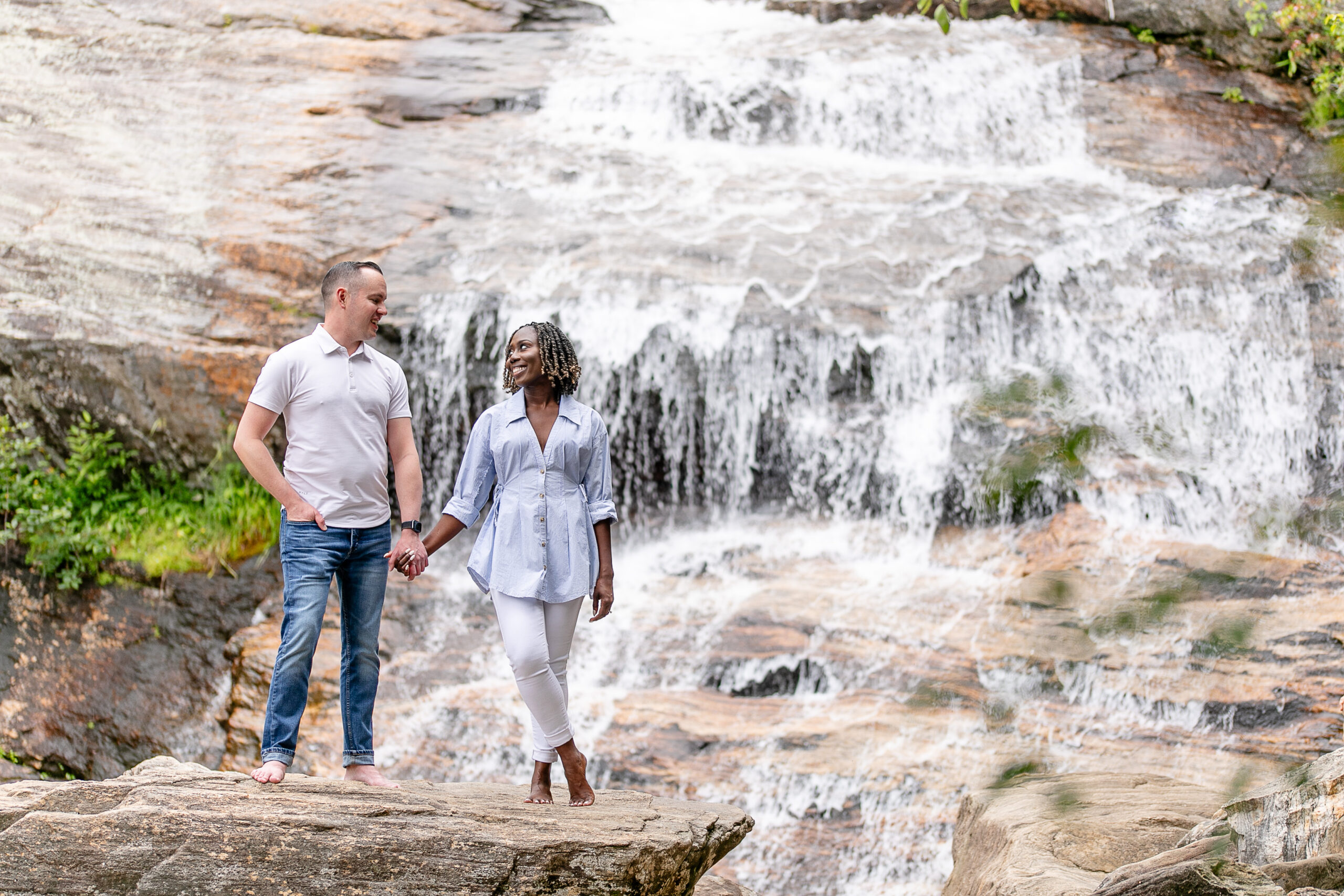 a man and a woman looking at each other holding hands with a waterfall behind them 