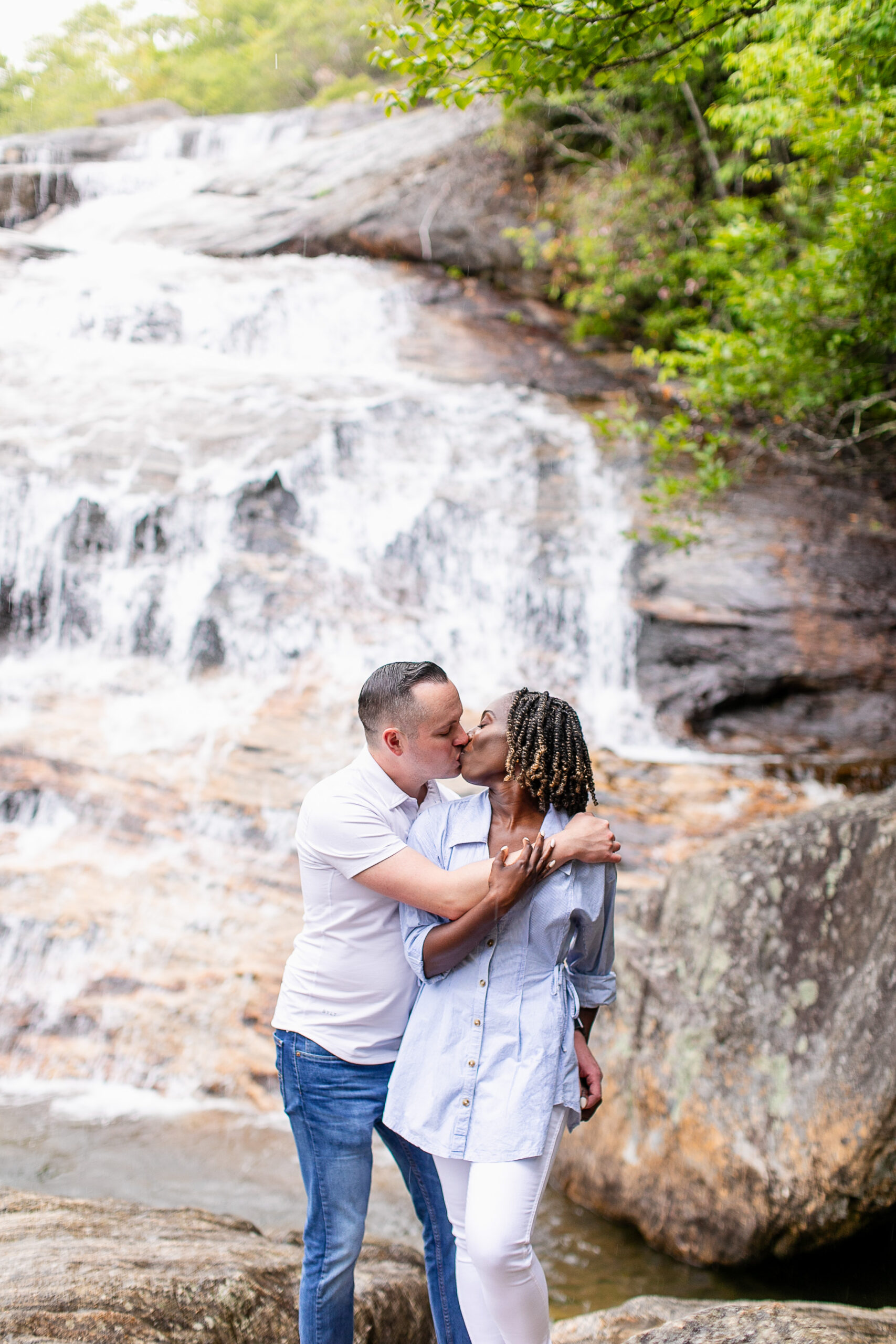 a man and a woman giving each other a kiss with a waterfall behind them