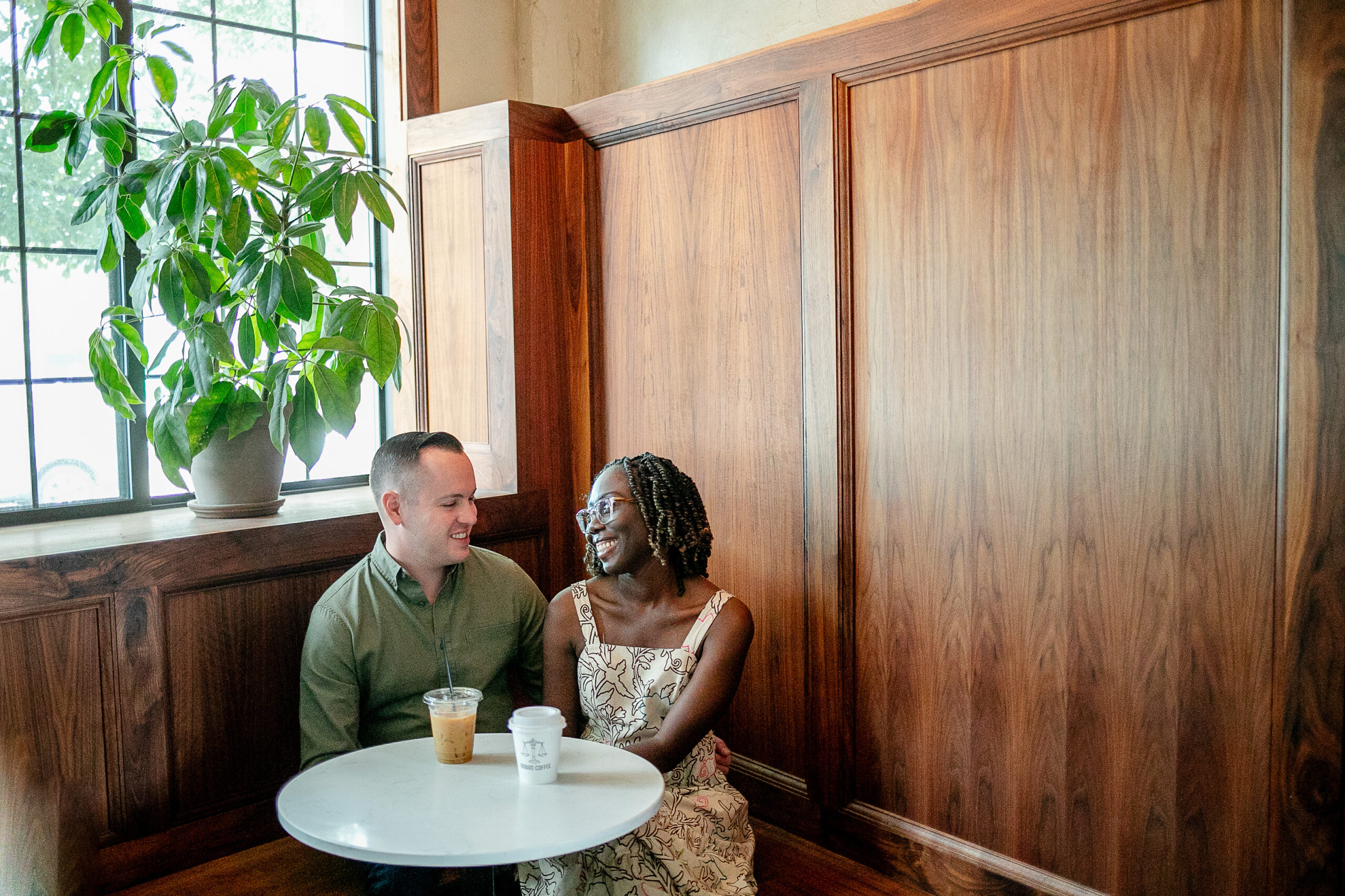 a man and a woman sitting tgoether in a coffee shop looking at each other and laughing 