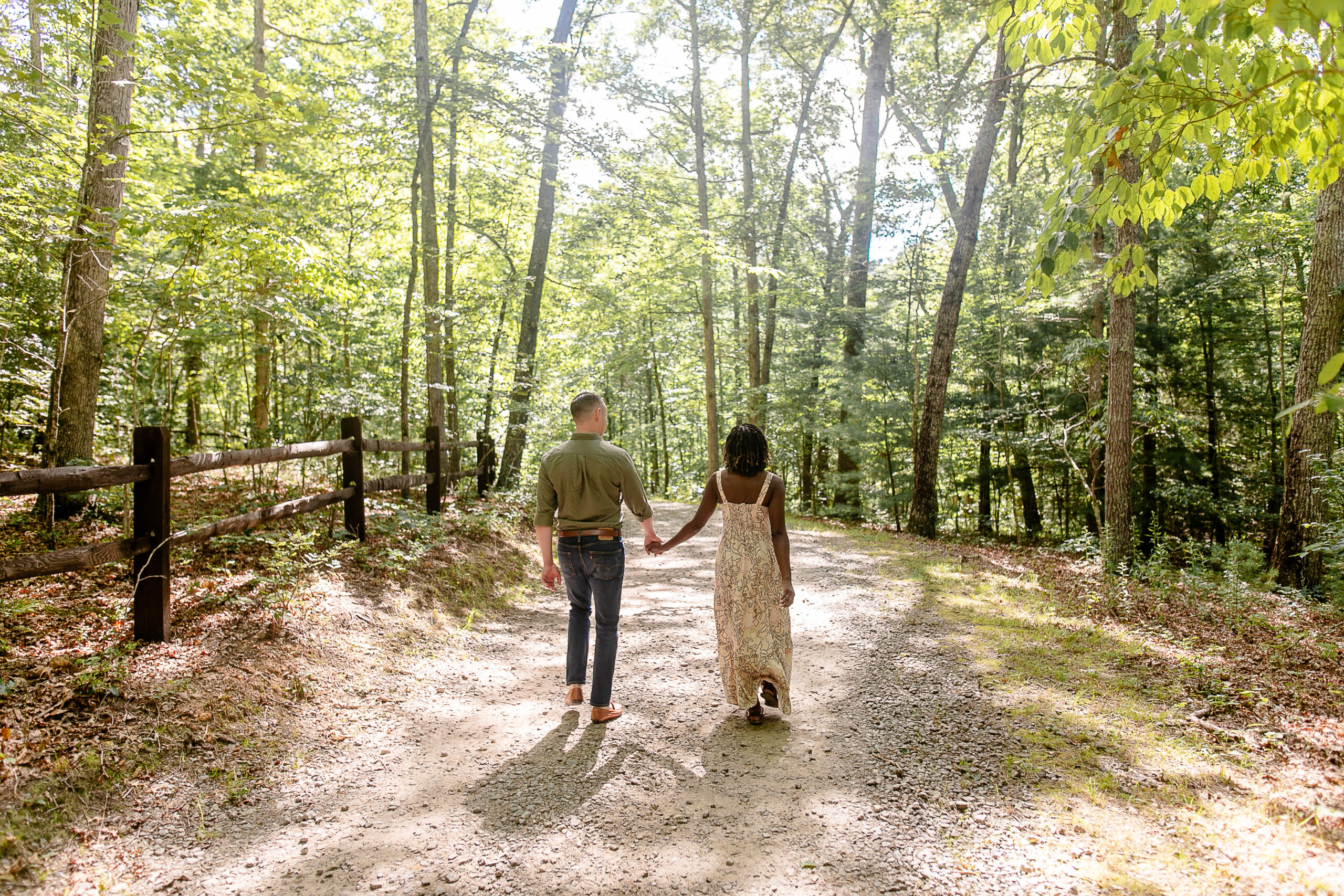 a woman and a male holding hands and walking down a path surrounded by trees 