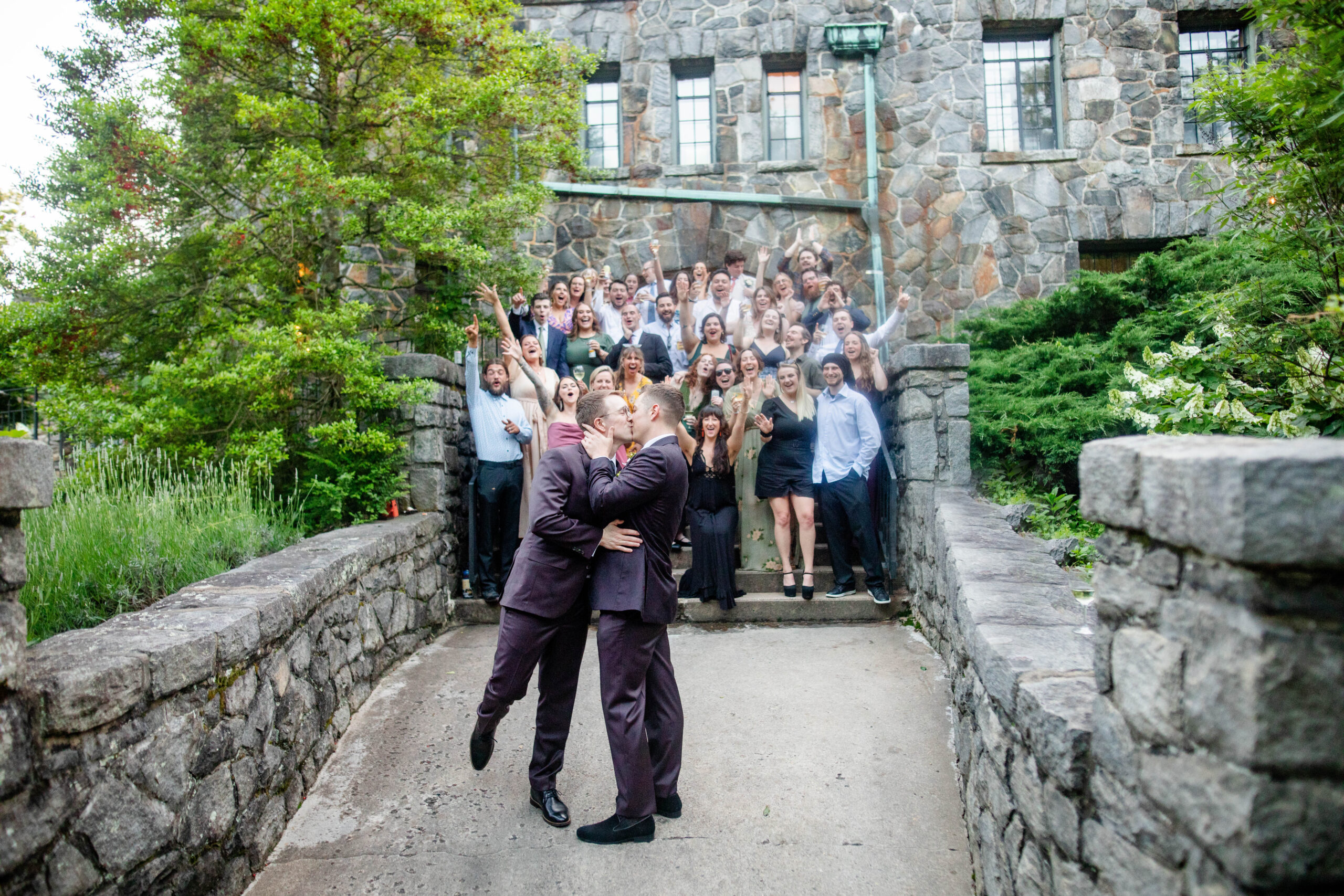 husbands giving each other a kiss as their wedding party cheers them on at Homewood wedding venue in Asheville