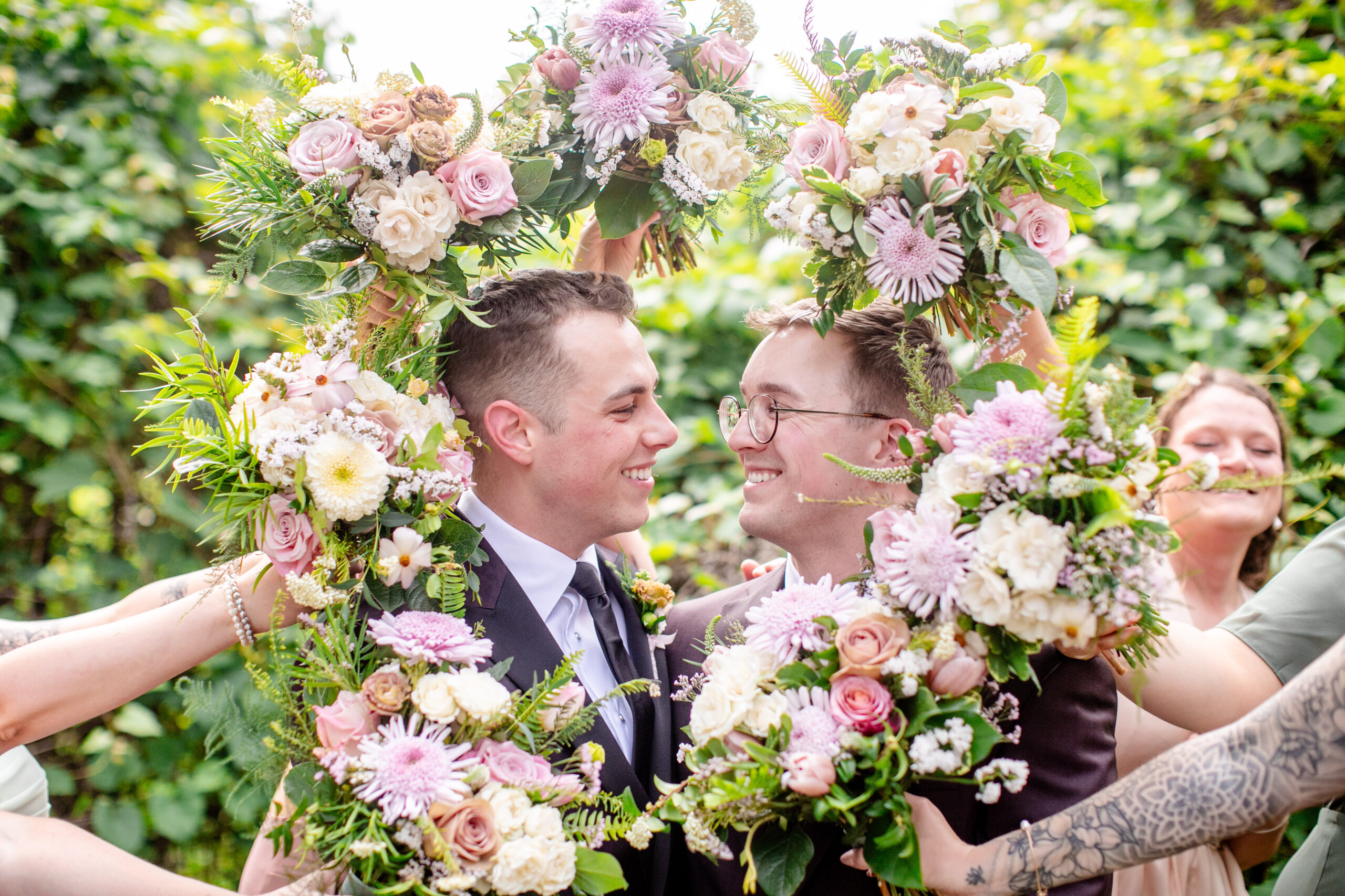 two men about to get married with flowers being held around their head by their wedding party 