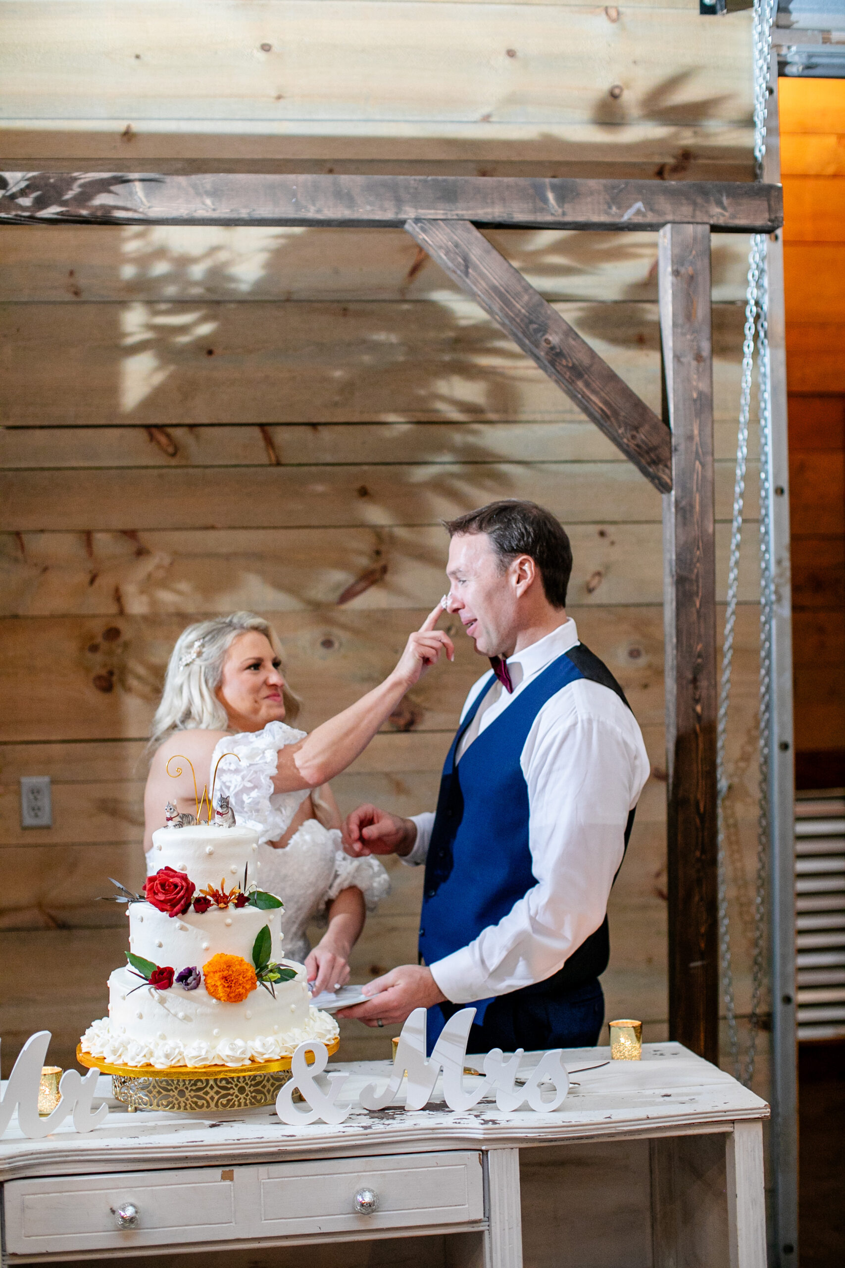 bride putting cake on her husband's nose with the wedding cake and table in front of them 