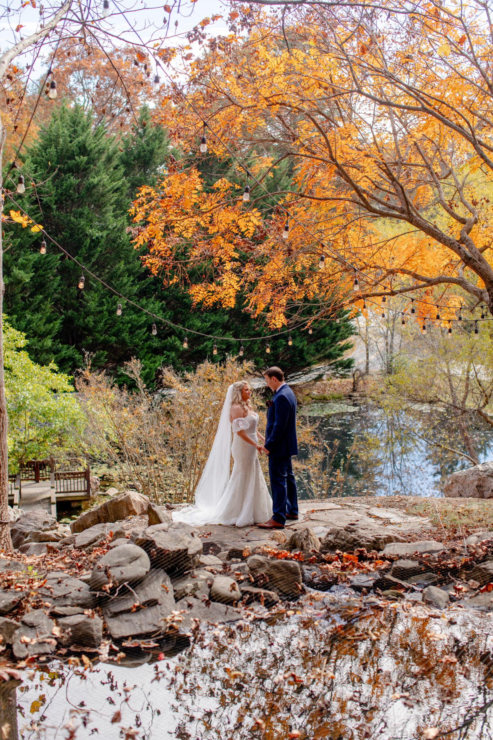 bride and groom looking at each other surrounded by fall foliage and lights 