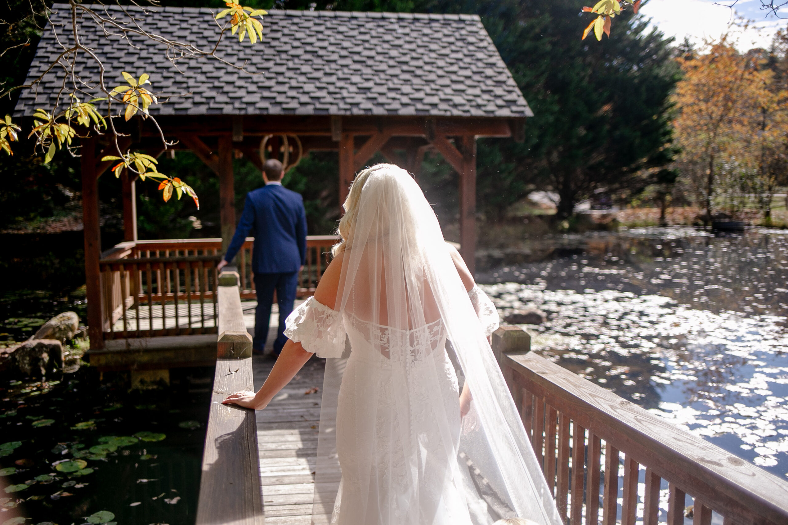 bride behind the groom on a bridge walking towards him