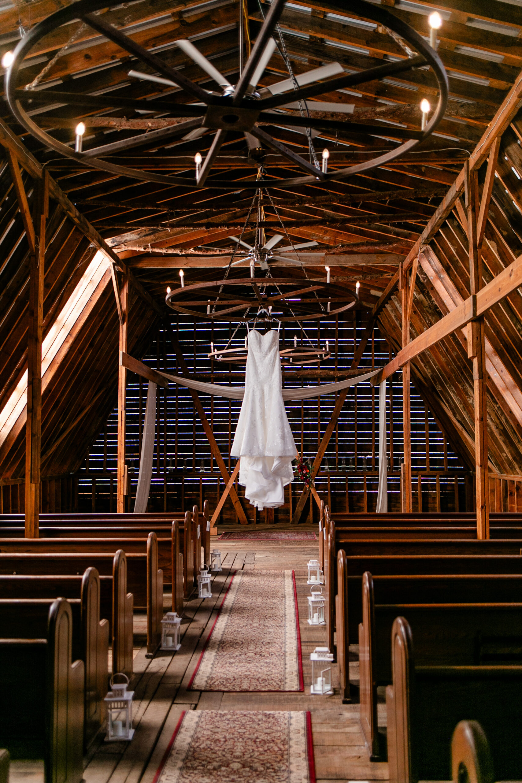 Honeysuckle Hill ceremony hall with wooden pews, chandeliers, and the bride's wedding dress hanging from a chandelier