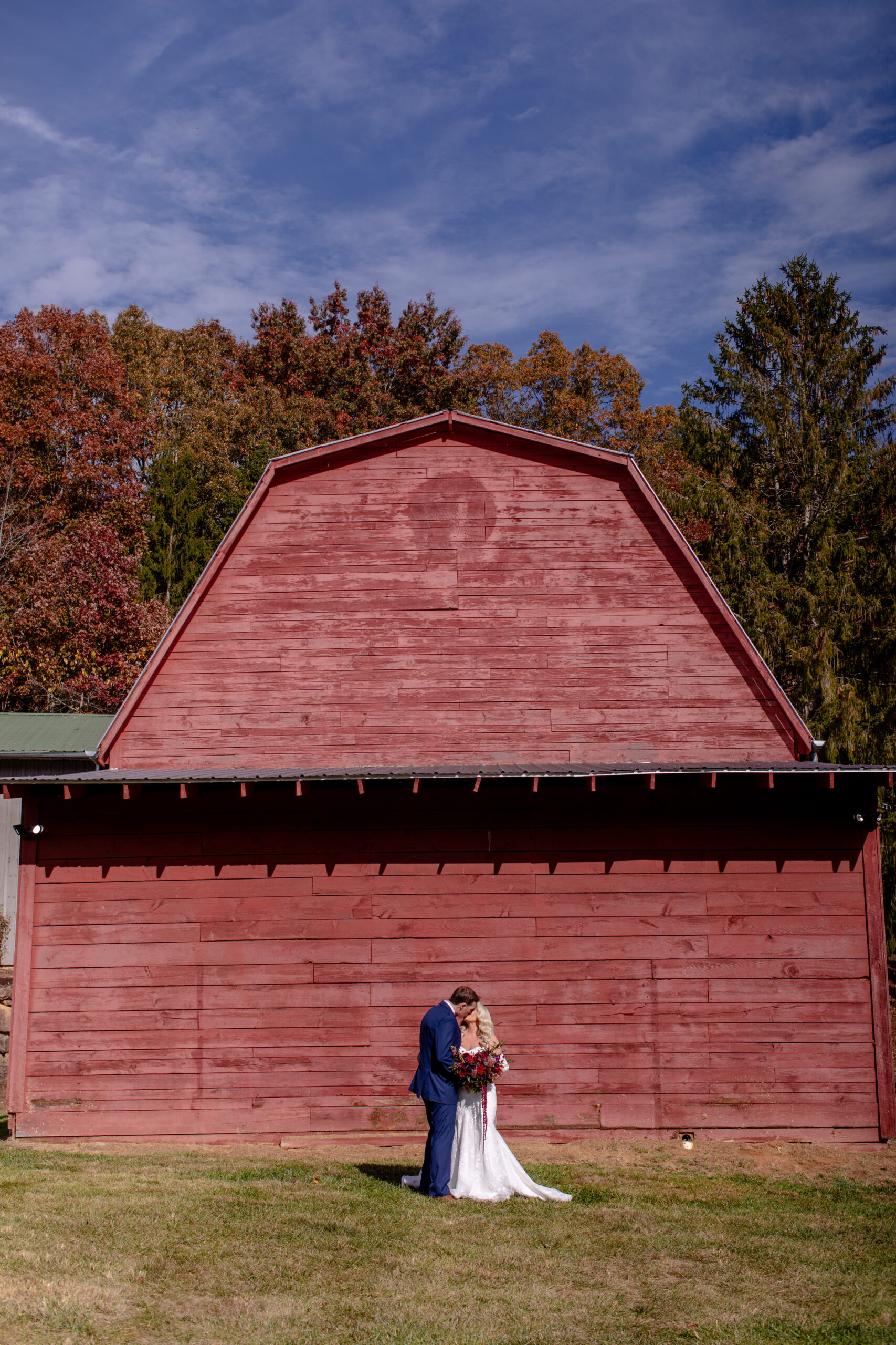 bride and groom kissing in front of a red barn 