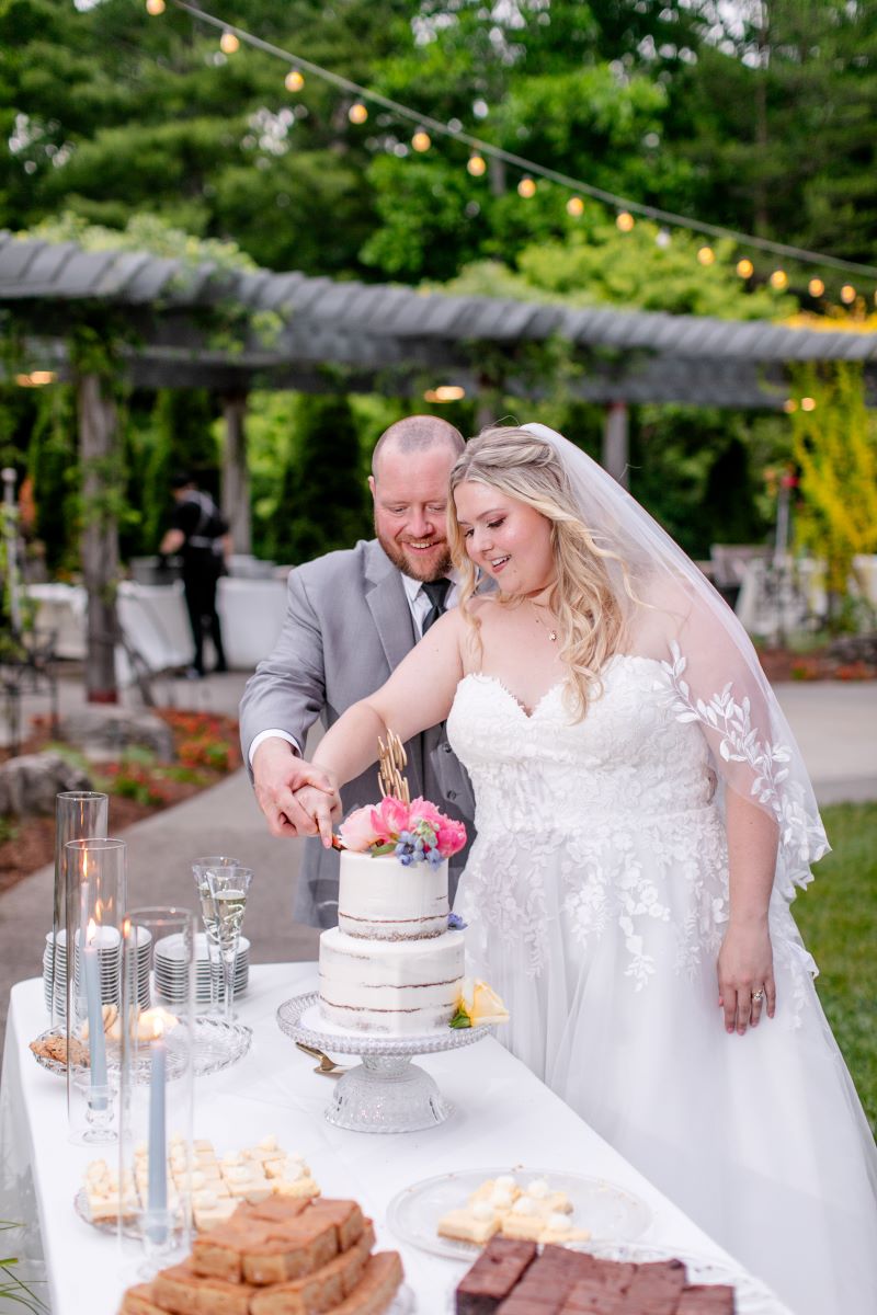 a man and woman cutting a wedding cake the woman is wearing a white wedding dress and the man is wearing a gray suit 