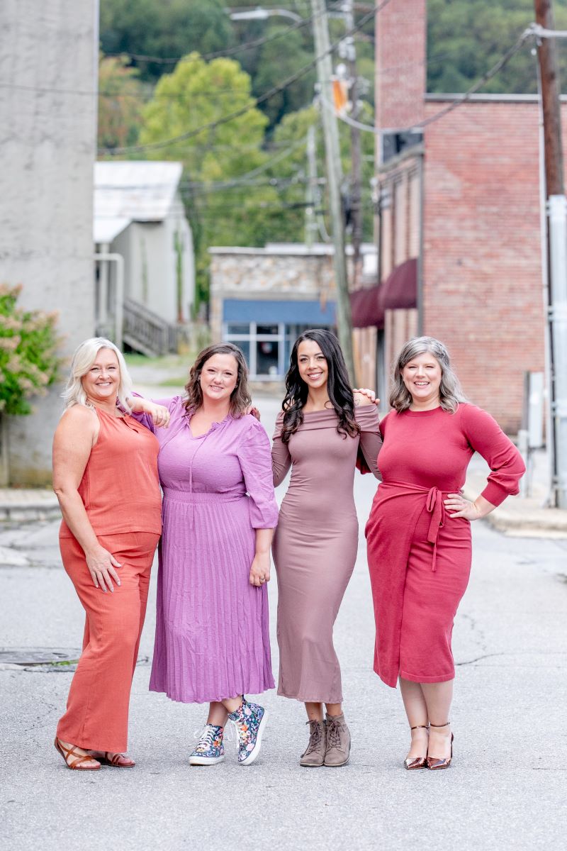 a group of women posing for a picture on a street they are all smiling and wearing dresses 