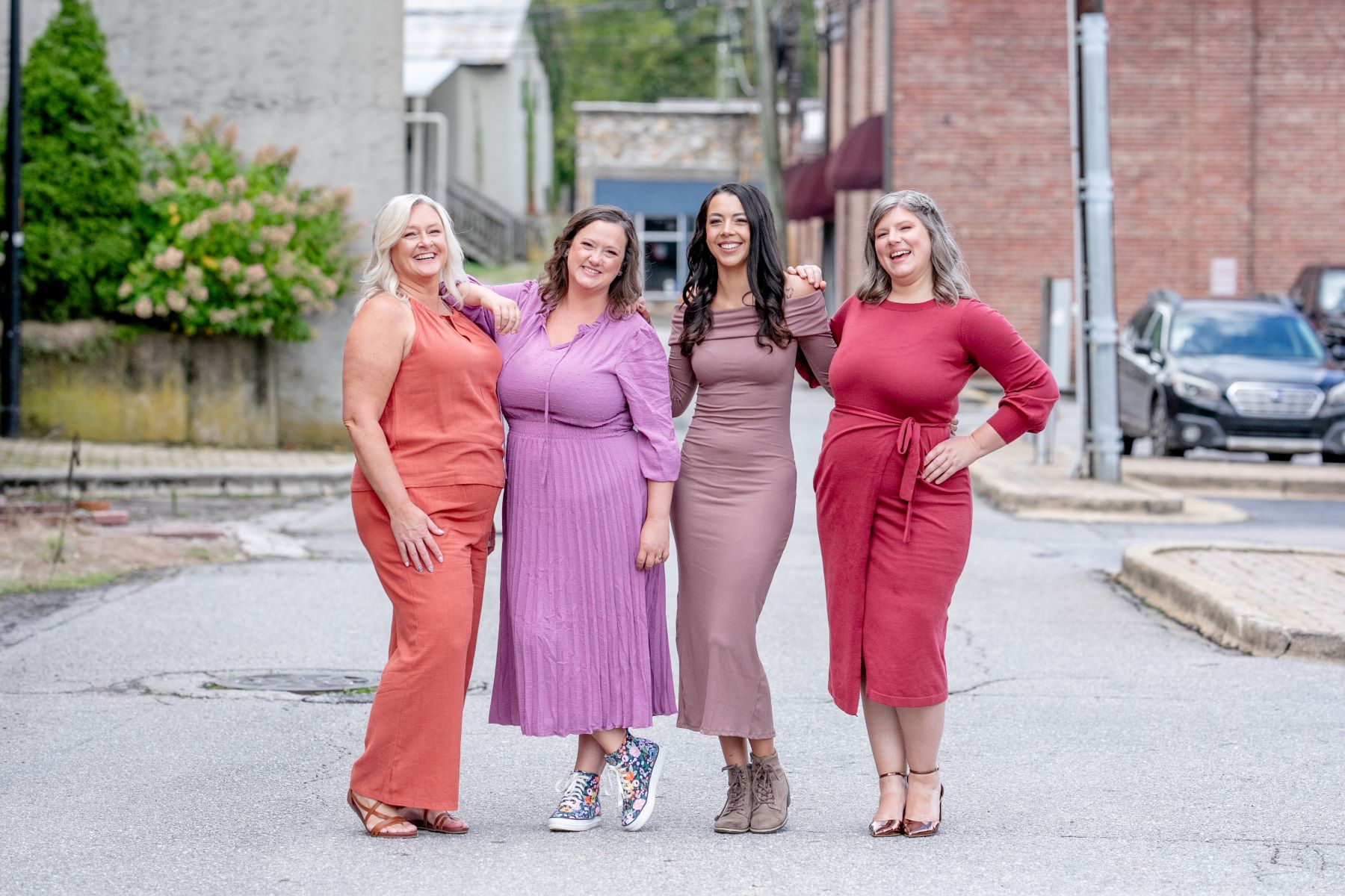 a group of women posing for a picture on a street and they are all wearing dresses and smiling