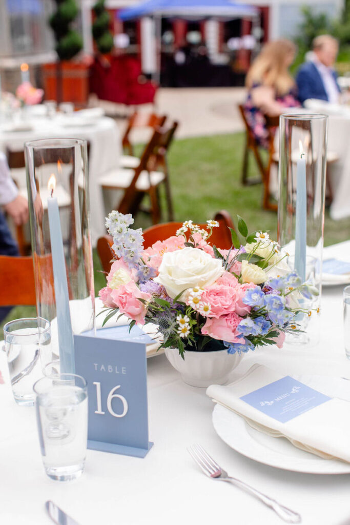 A wedding reception table with a floral bouquet, candles, a table number, and flatware. 