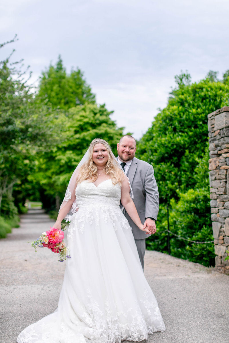 A newlywed couple smiling and holding hands after their North Carolina Arboretum Wedding