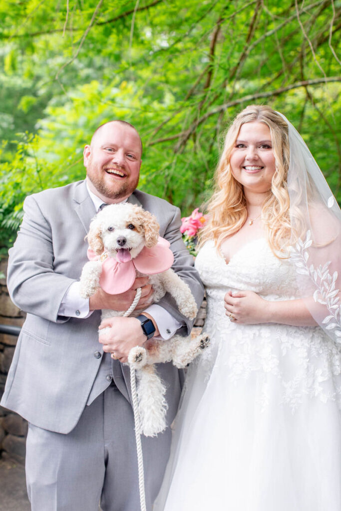 Newlyweds smiling as one of them holds a dog. 