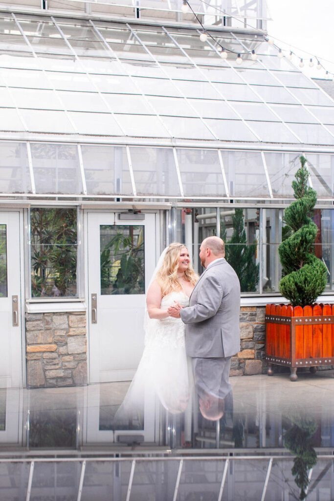 A newlywed couple during their first dance in front of a greenhouse