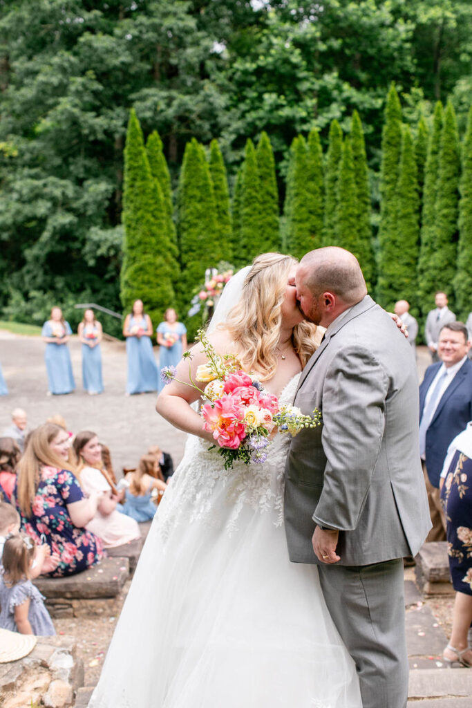 Newlywed couple kissing with their wedding guests looking on 