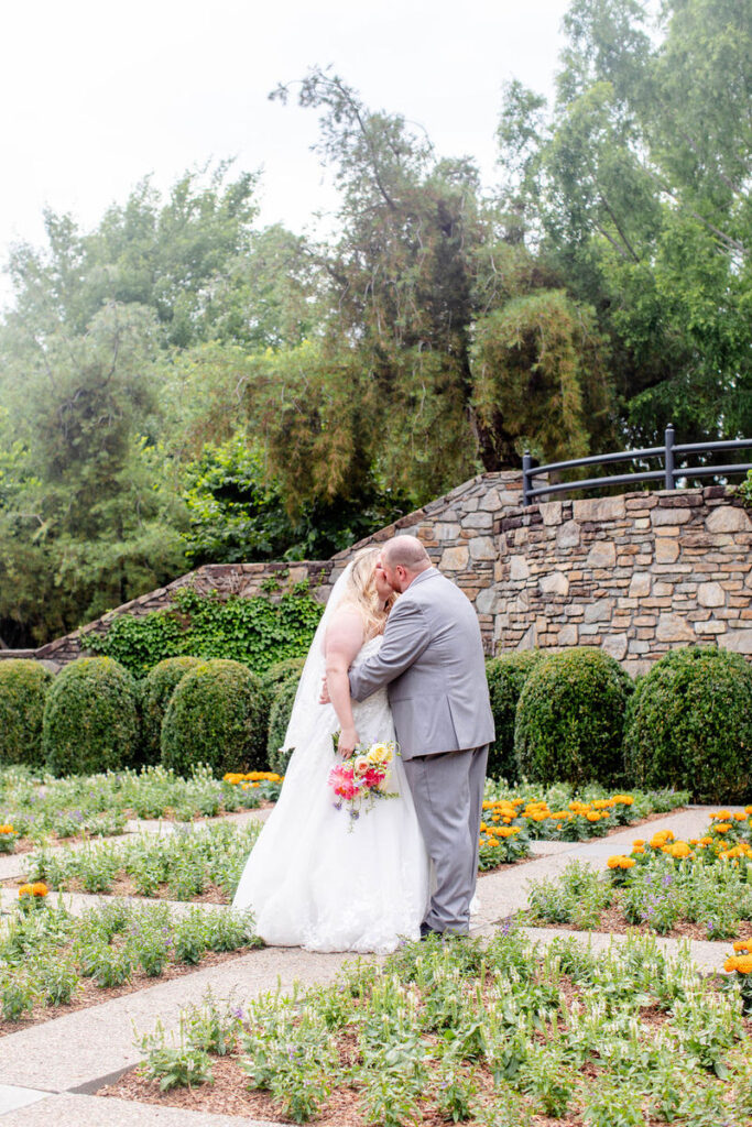 A couple in wedding outfits kissing in a garden. 