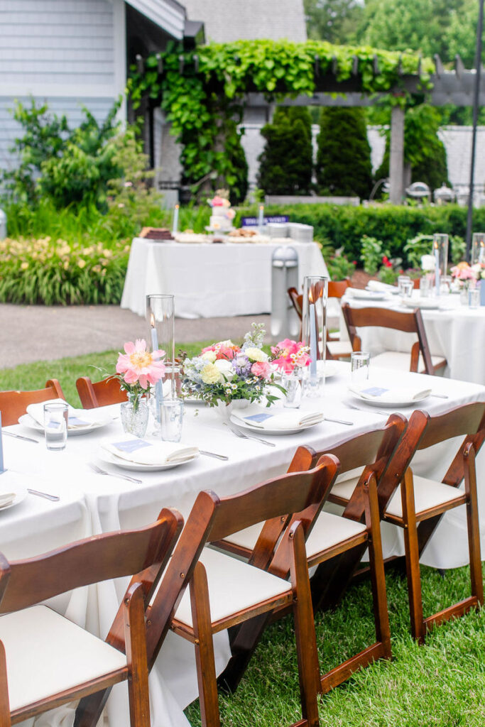 Wooden chairs around a rectangular wedding reception table on a lawn. 