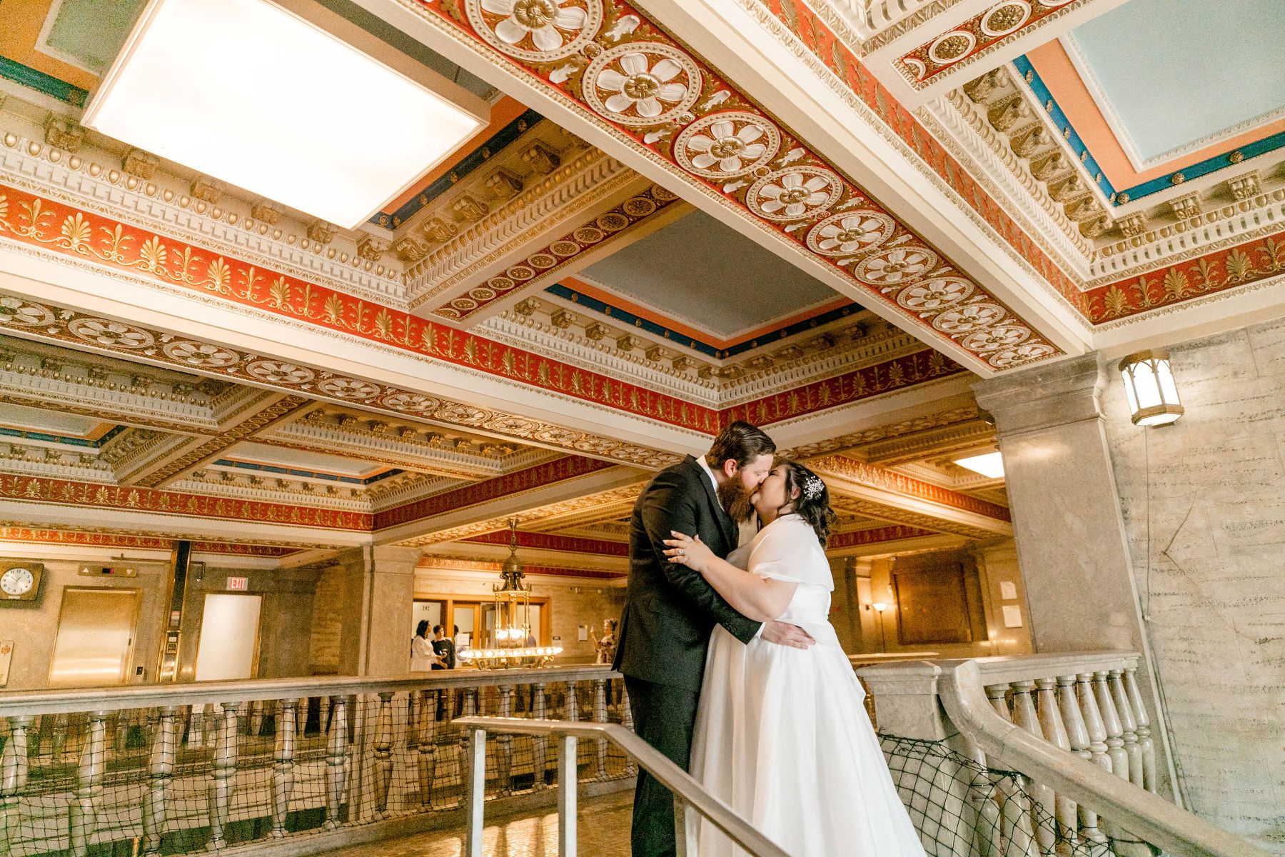 a man and woman kissing in a building the woman is wearing a white dress the man is wearing a black suit they are standing on top of a staircase