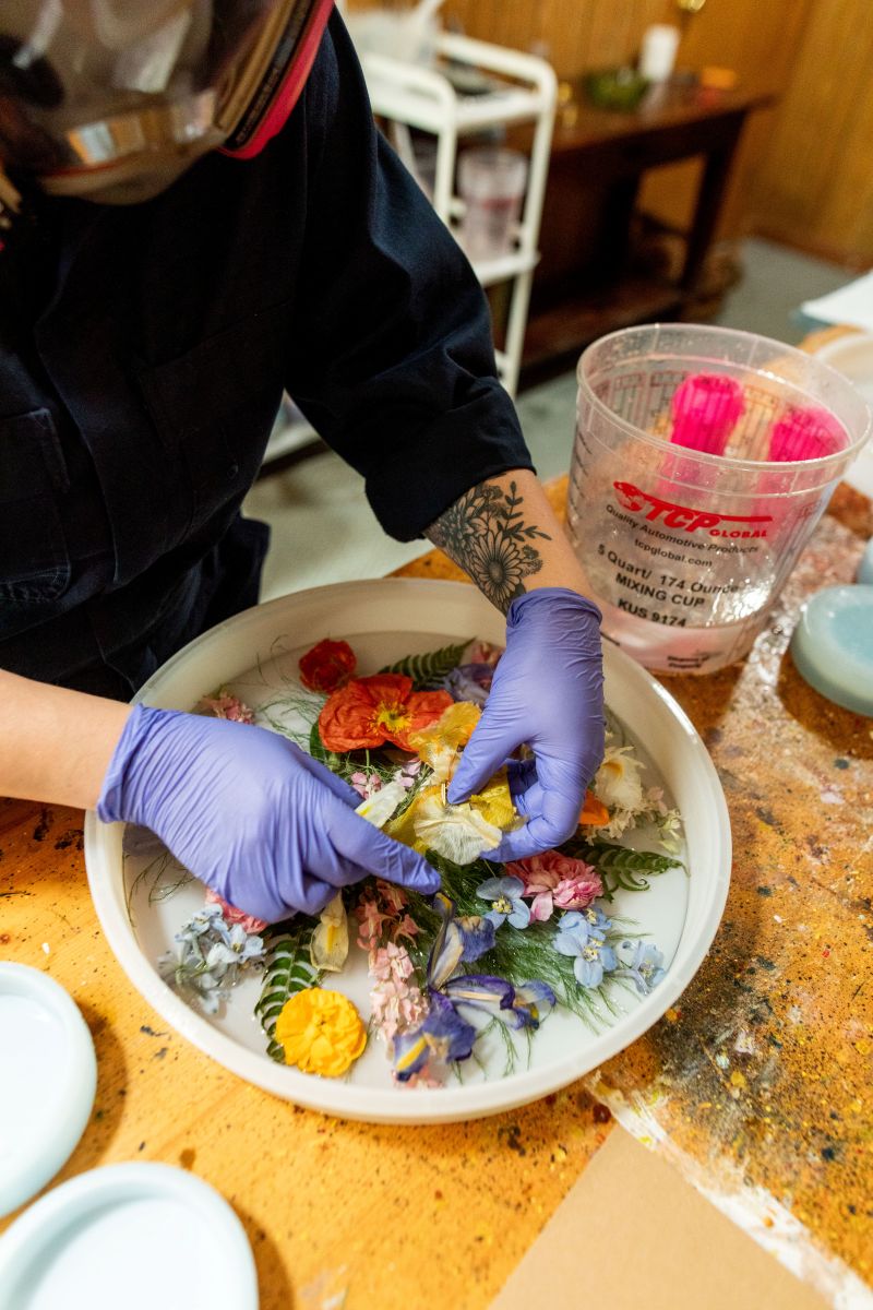 a woman in her wokspace wearing a gas mask working to preserve flowers 