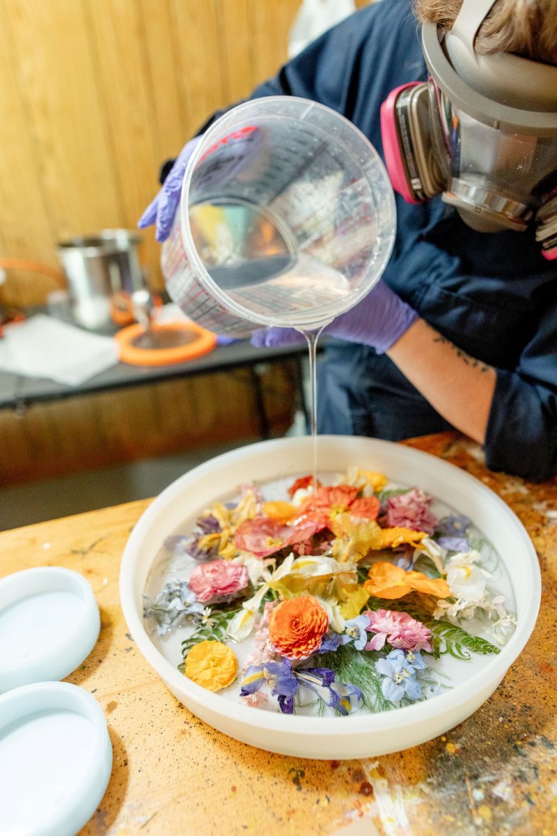 a woman wearing a gas mask pouring a clear liquid over flowers she is working to preserve 