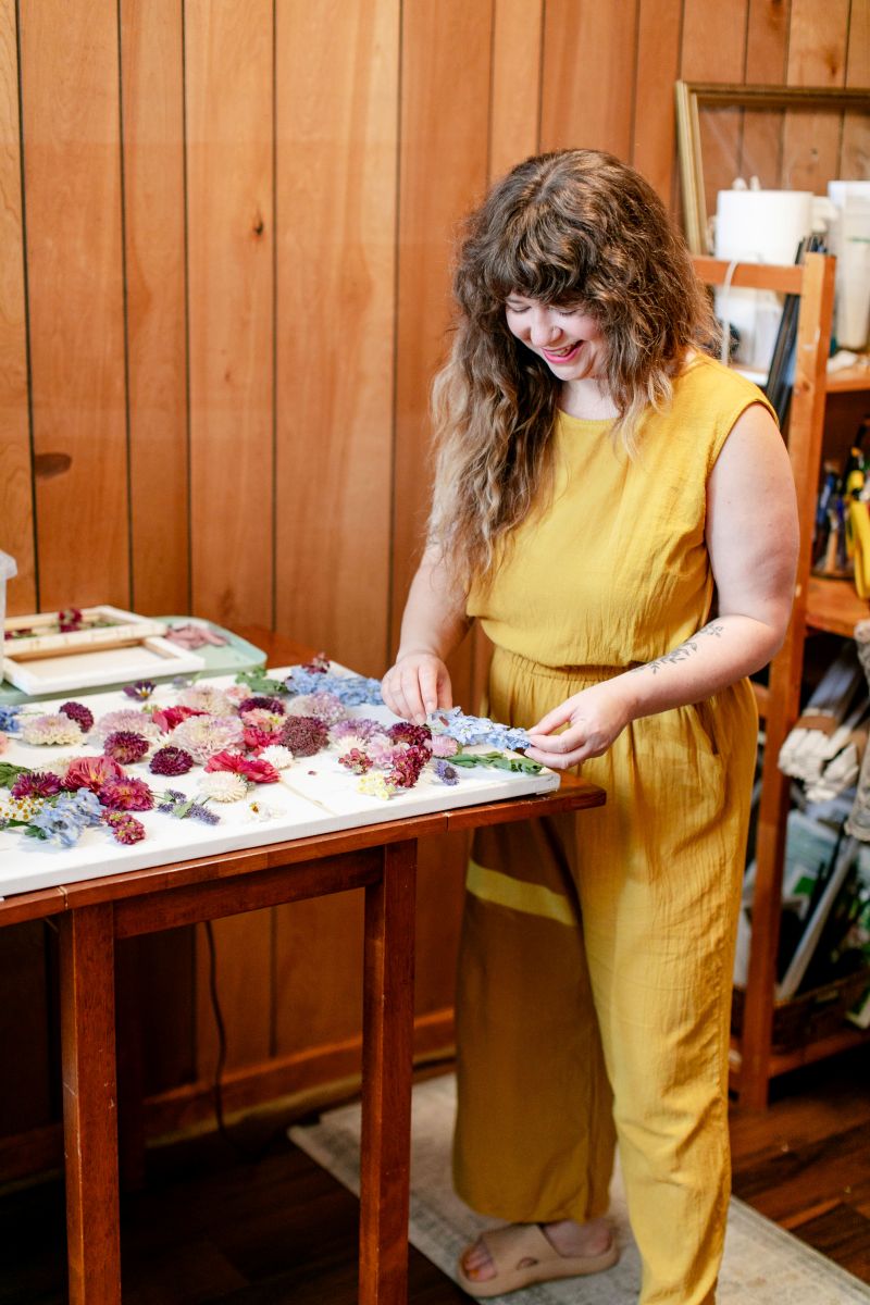 A woman in a yellow jumper working in her workspace preserving flowers 