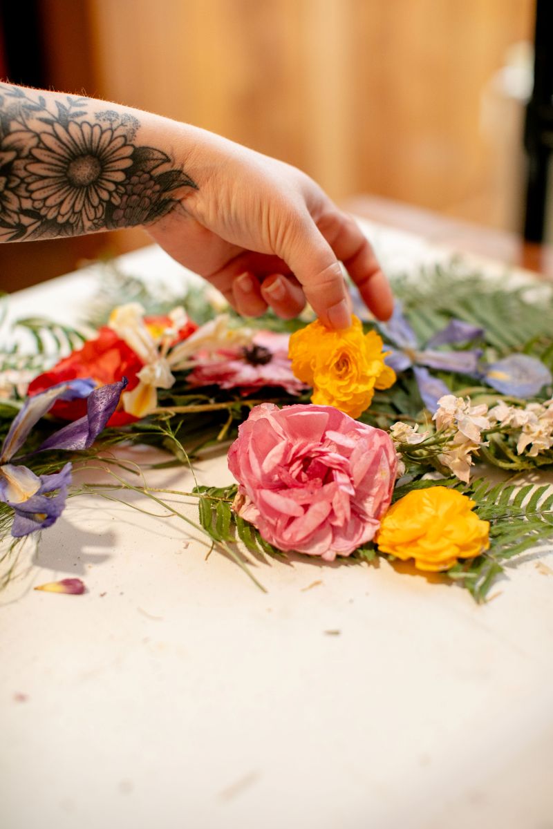 A woman holding up a flower in her workshpace on the table are other flowers 