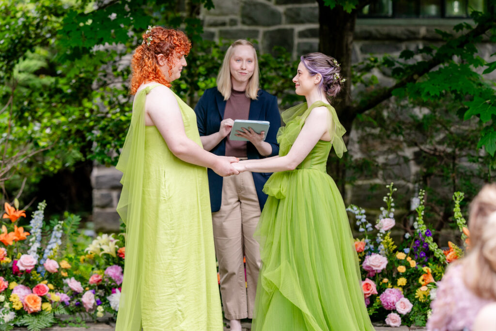LGBTQ friendly wedding photographer Asheville capturing two brides holding hands during their outdoor ceremony surrounded by colorful flowers at Homewood