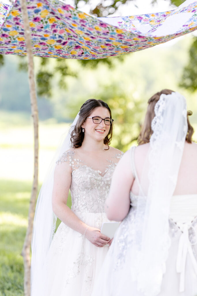 LGBTQ friendly wedding photographer Asheville capturing two brides exchanging vows under a colorful floral chuppah during their outdoor ceremony