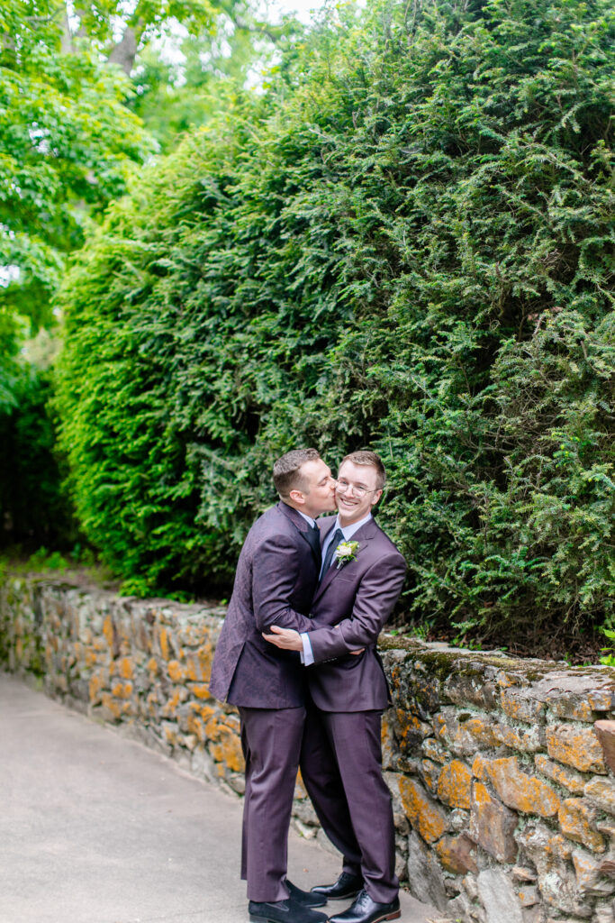 LGBTQ friendly wedding photographer Asheville capturing two grooms embracing and laughing along a stone path surrounded by lush greenery
