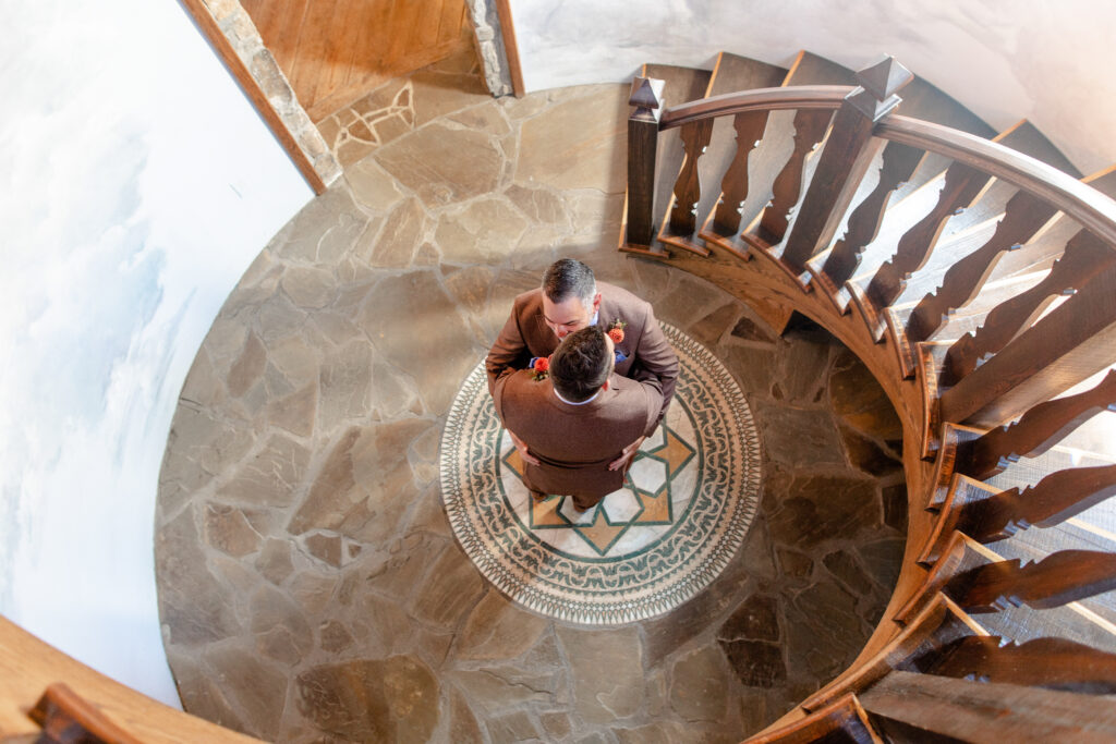 LGBTQ friendly wedding photographer Asheville capturing two grooms embracing at the bottom of a spiral staircase with a decorative mosaic floor